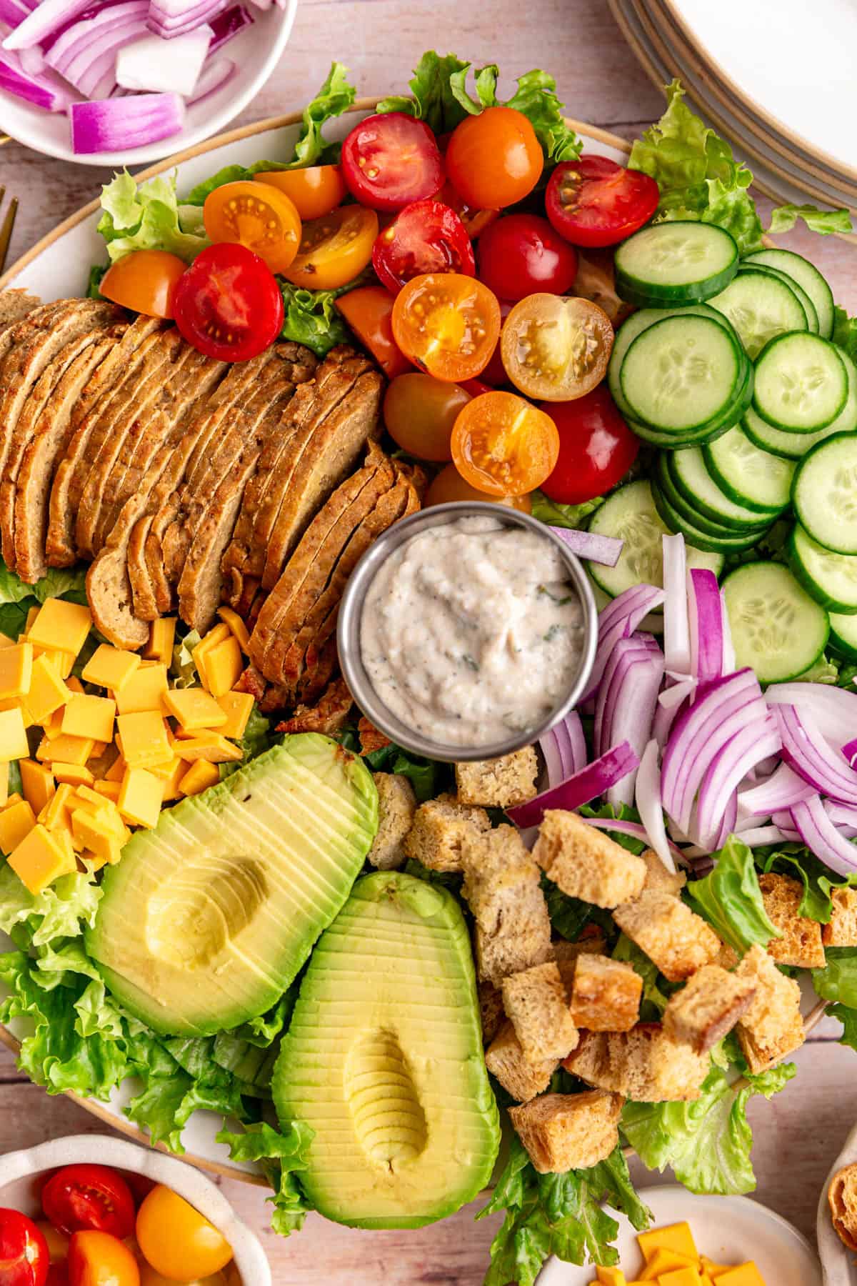A platter of Vegan Chef Salad surrounded by small bowls of salad ingredients.