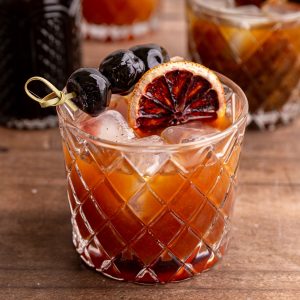 A whiskey sour mocktail garnished with a dried blood orange and cocktail cherries.