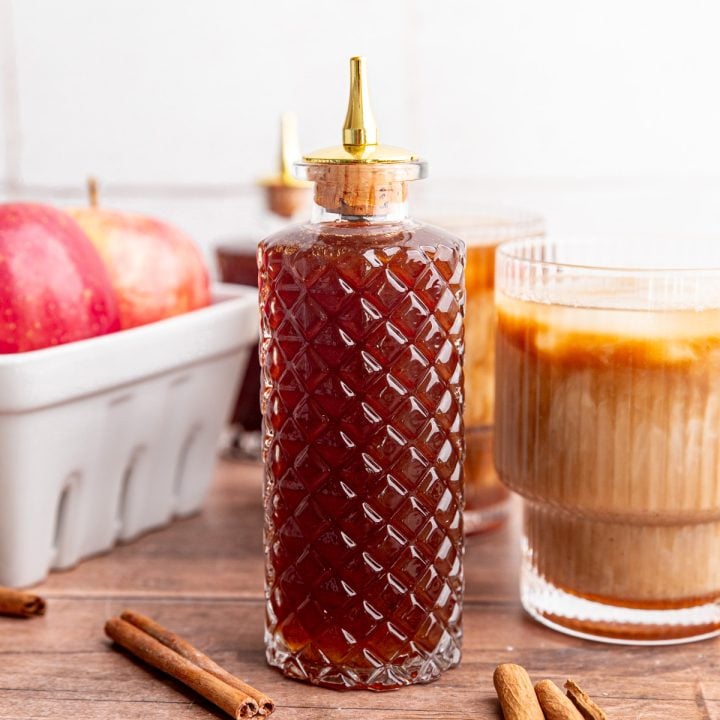 A bottle of brown sugar apple crisp syrup next to an apple crisp latte.