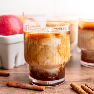 An iced Apple Crisp Latte on a table next to a basket of apples.