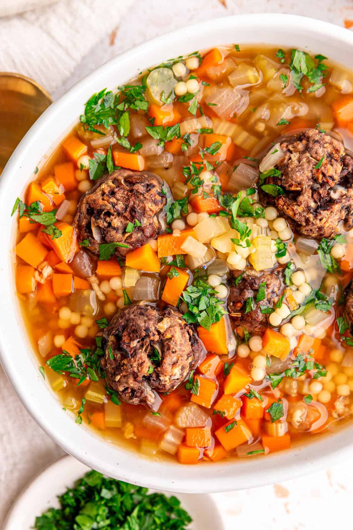 A close up view of a bowl of vegan Italian wedding soup, and seitan meatballs.