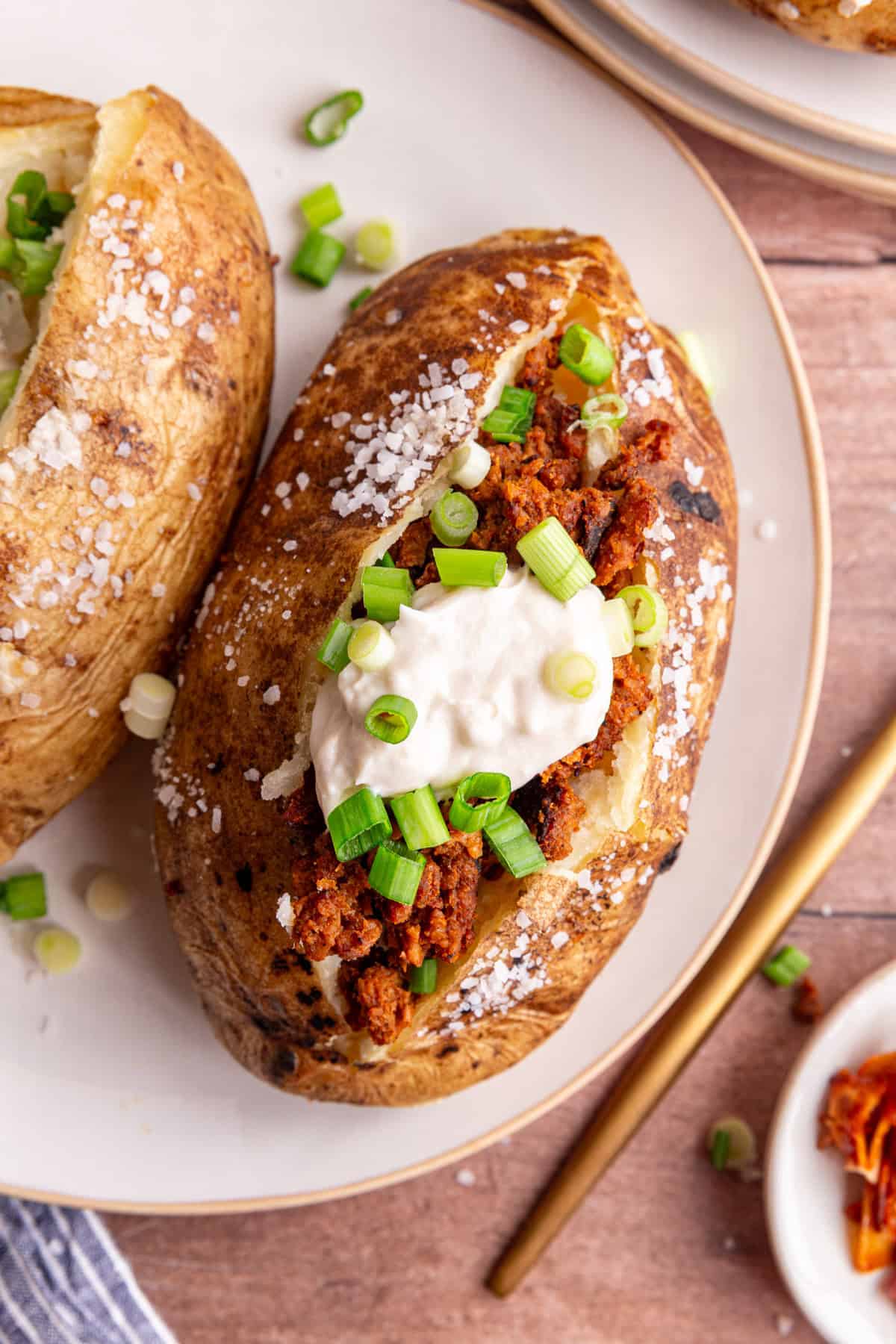 A baked potato with vegan chorizo, vegan sour cream, and scallions.