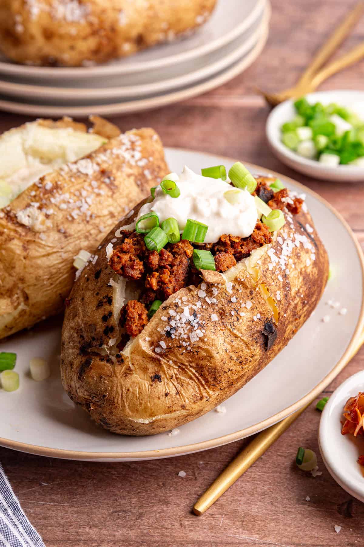 A baked potato with vegan chorizo, vegan sour cream, and scallions.