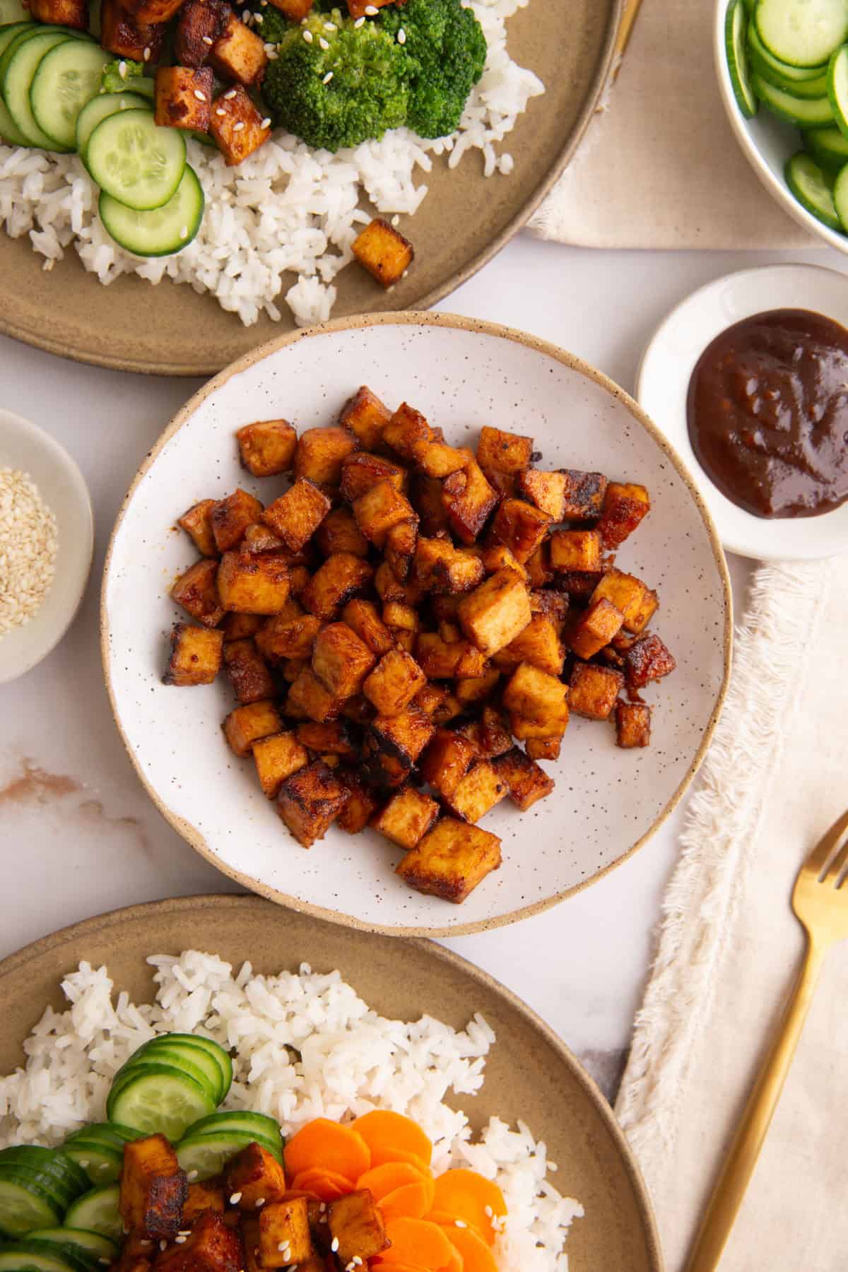 A bowl of hoisin tofu, next to two plated meals.