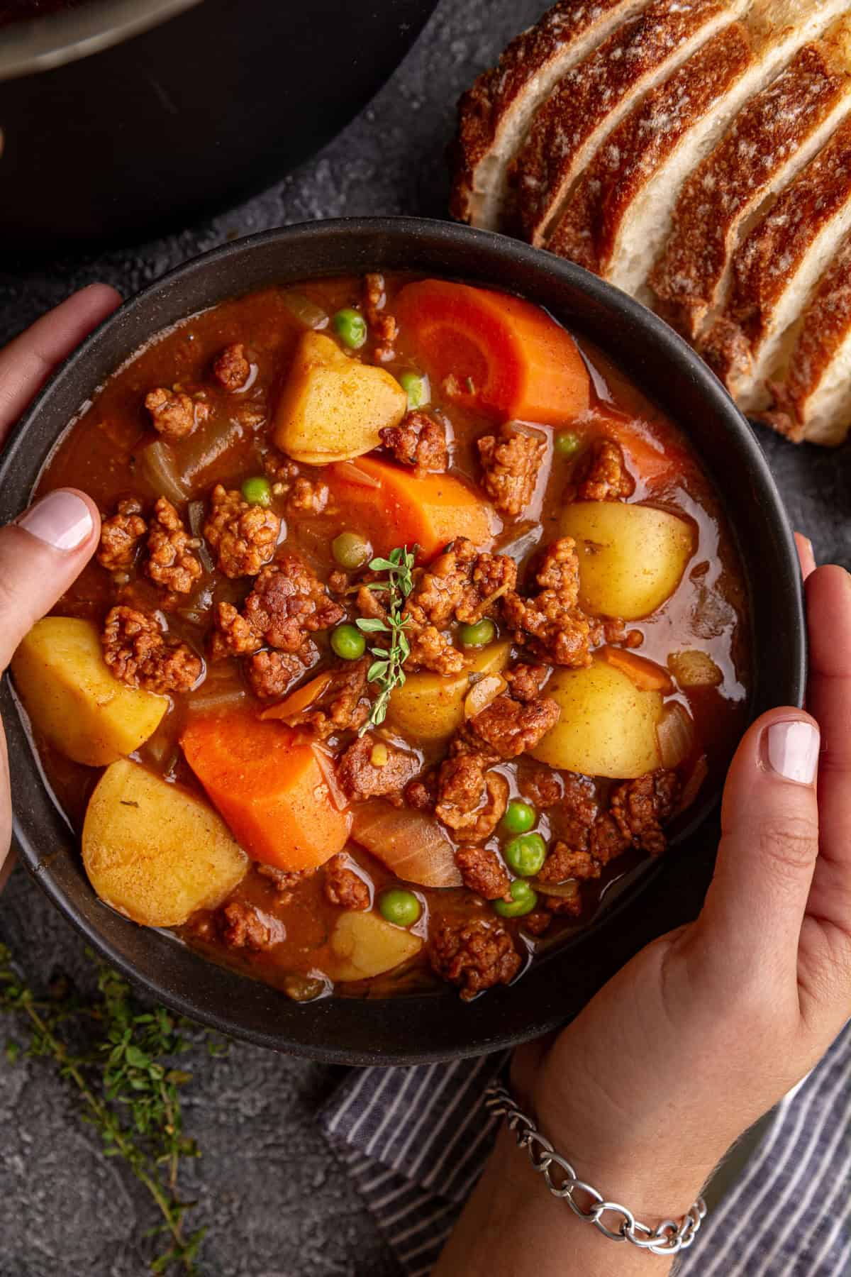 Hands around a bowl of vegan chorizo stew.
