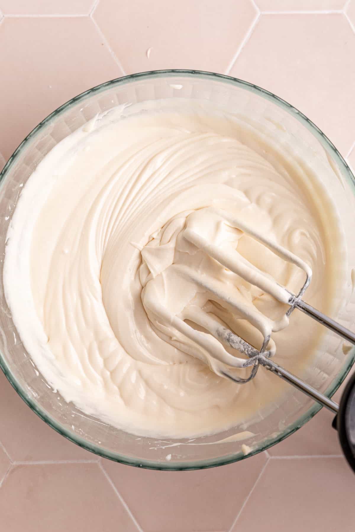 A bowl of Vegan Cream Cheese buttercream Frosting, with the beaters still in the bowl.