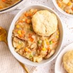A bowl of vegan pot pie soup, with a biscuit on top.