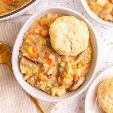 A bowl of vegan pot pie soup, with a biscuit on top.
