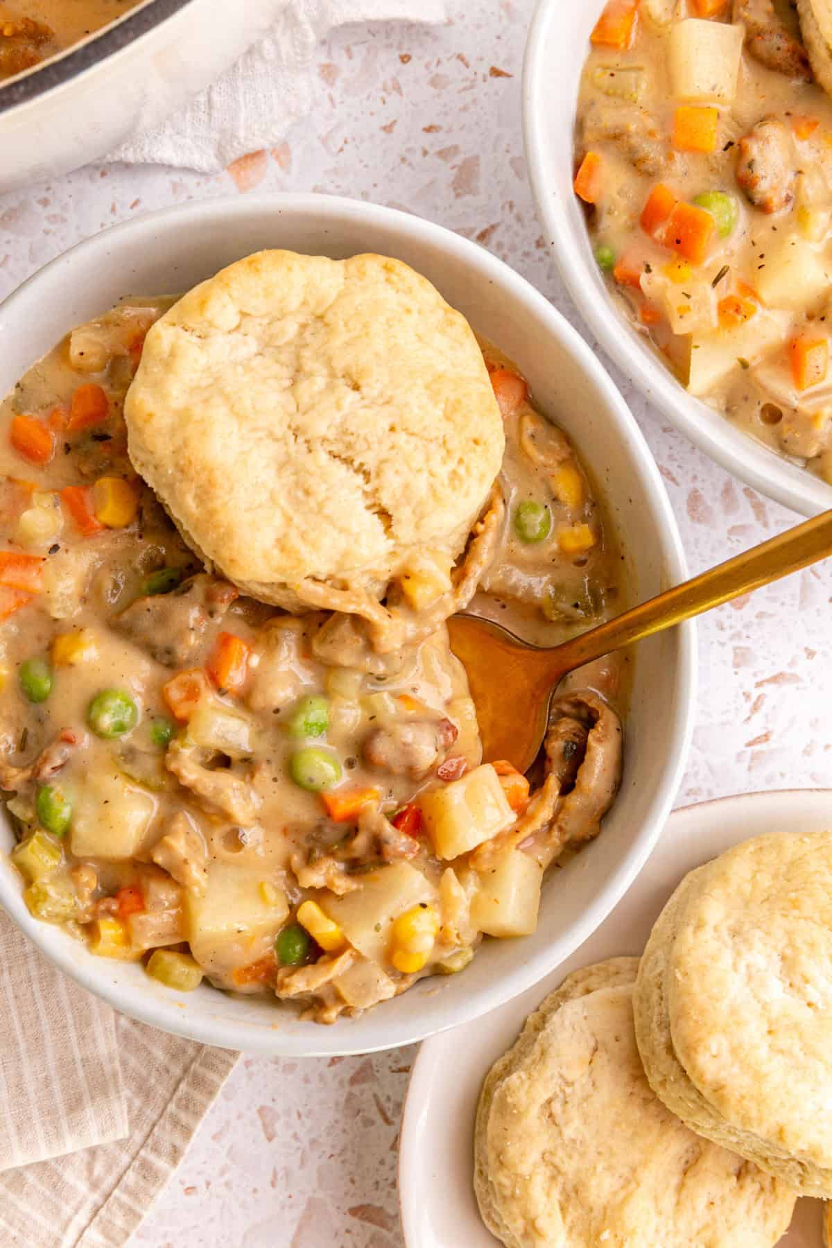 A bowl of vegan pot pie soup, with a biscuit on top, and a spoon scooping into the soup.