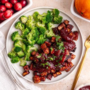 A plate of Cranberry Orange Tofu, topped with more sauce, and a side of broccoli.