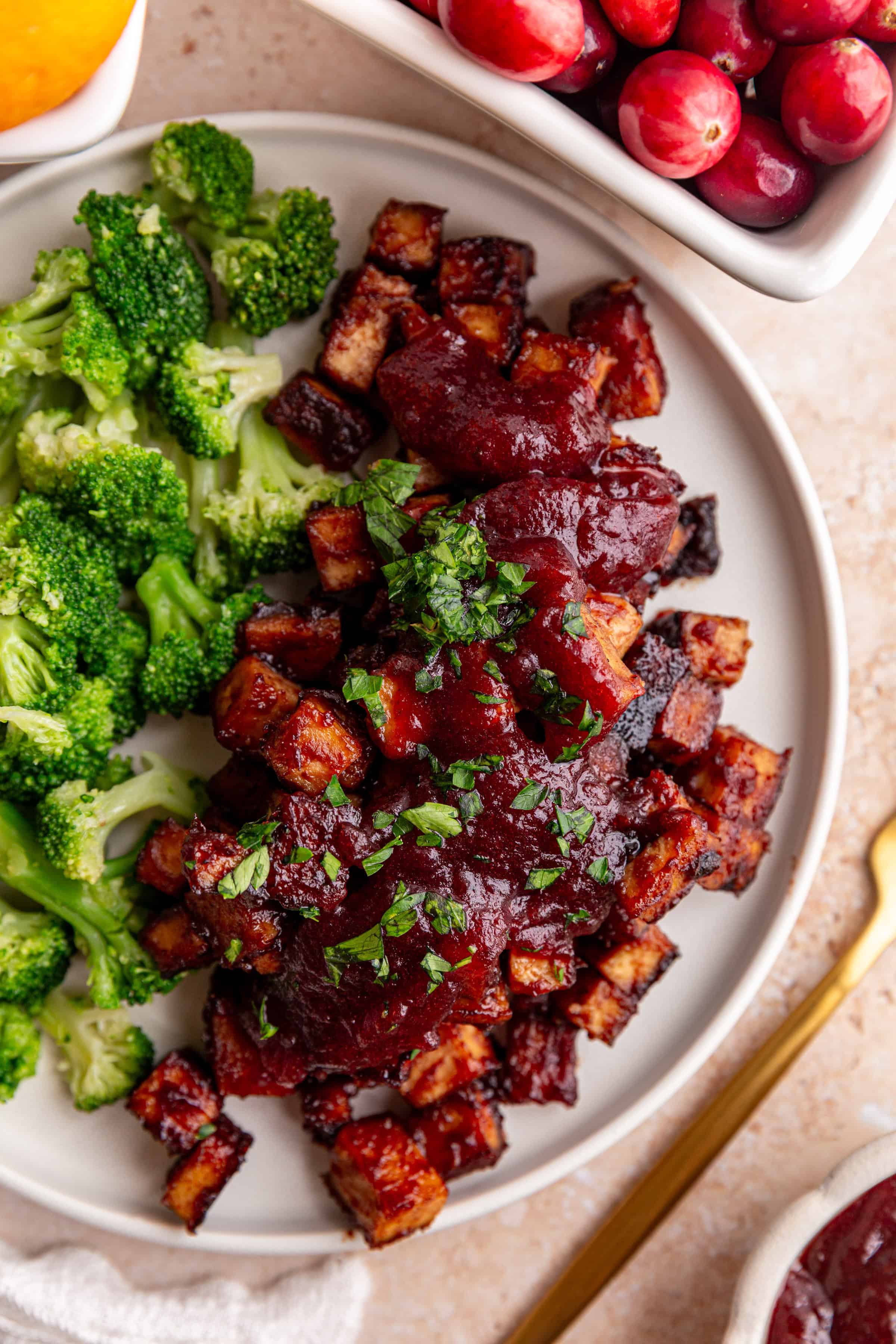 A plate of Cranberry Orange Tofu, topped with more sauce, and a side of broccoli.