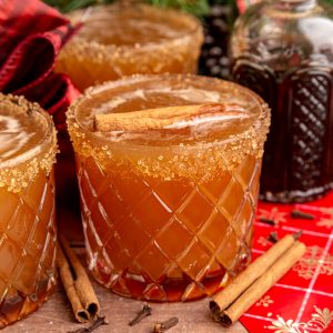 A gingerbread mocktail in a whiskey glass, rimmed with sugar and garnished with a cinnamon stick.