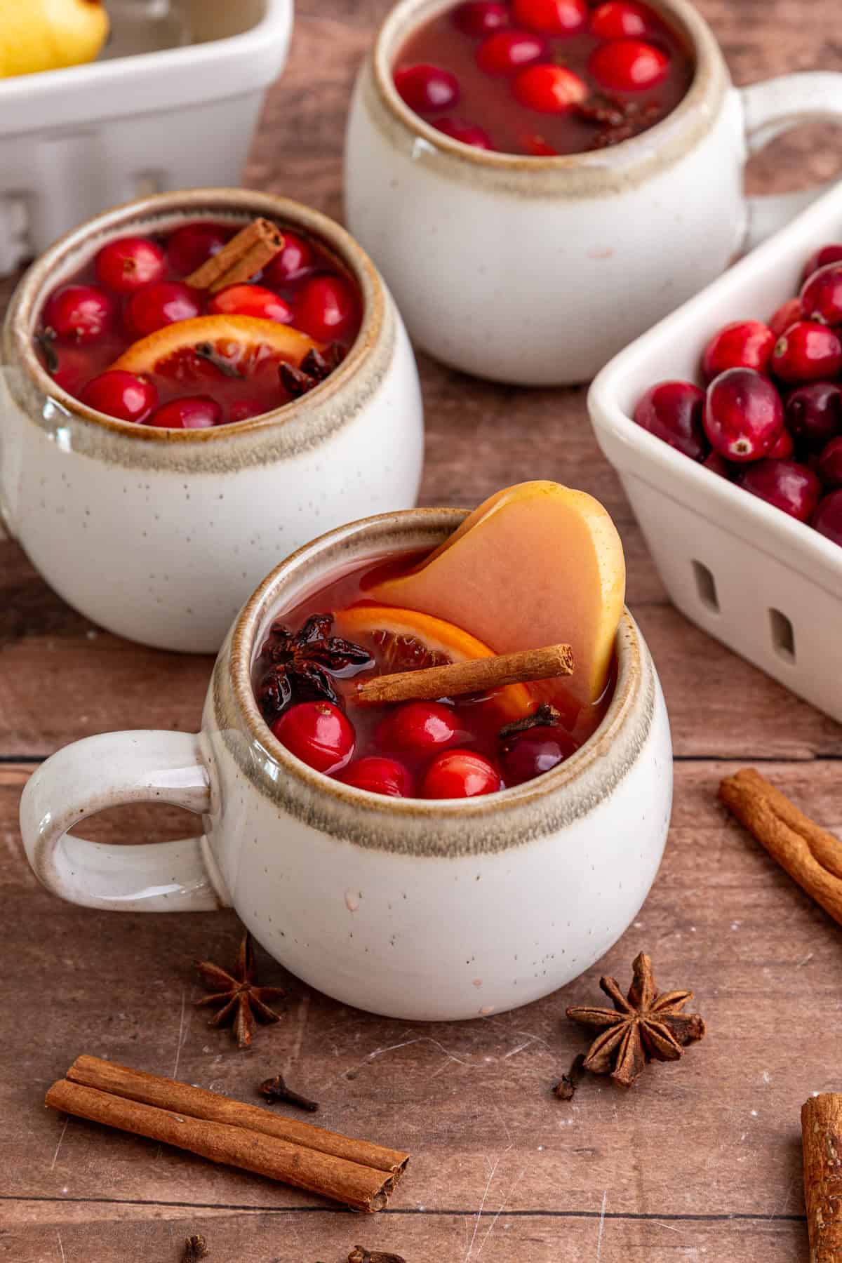 Three mugs of non alcoholic mulled wine, with fruits floating on top.