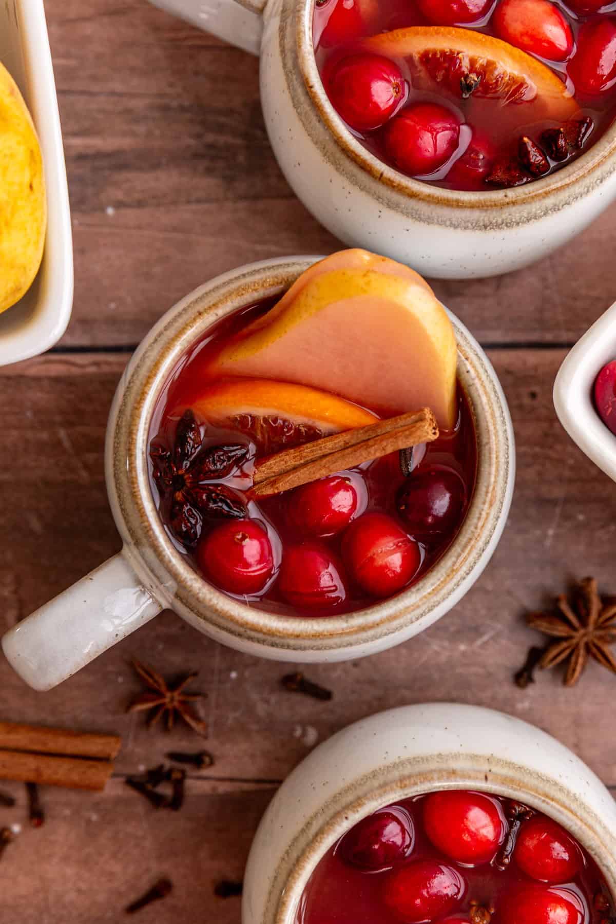 Three mugs of non alcoholic mulled wine, with fruits floating on top.