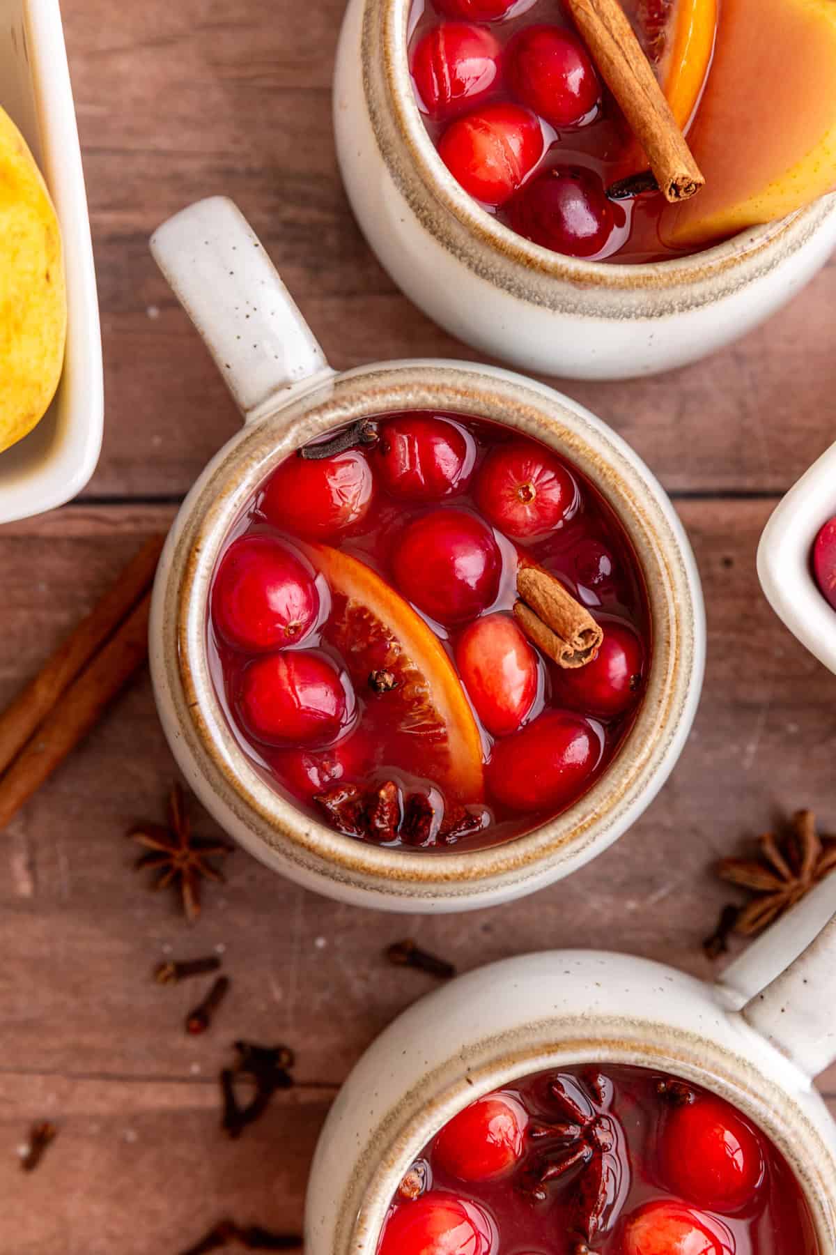 Three mugs of non alcoholic mulled wine, with fruits floating on top.