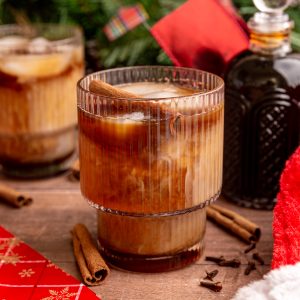 An iced vegan gingerbread latte garnished with a cinnamon stick.