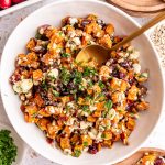 A bowl of Vegan Roasted Sweet Potato Salad with a spoon in it, ready to serve.