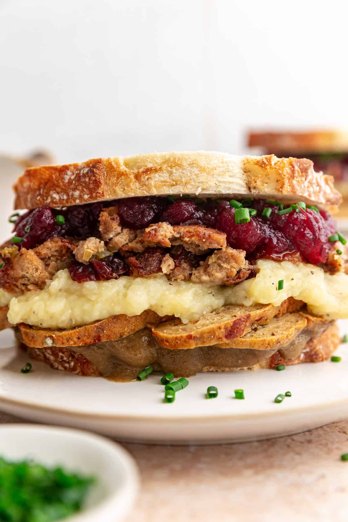 A Vegan Thanksgiving Leftovers Sandwich, loaded with stuffing, mashed potatoes, and cranberry sauce.