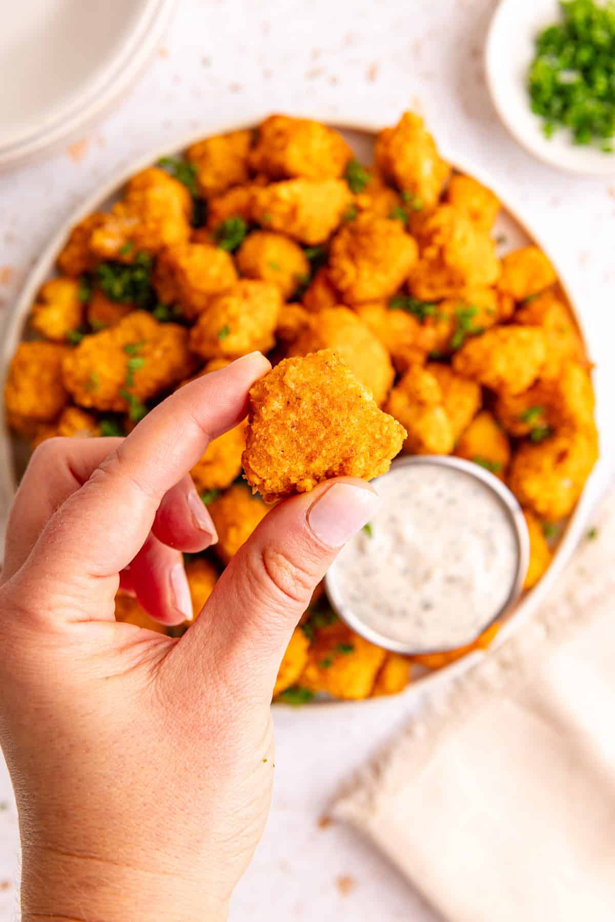 A hand holding a buffalo tofu popper to show the bite-size and crispy texture.