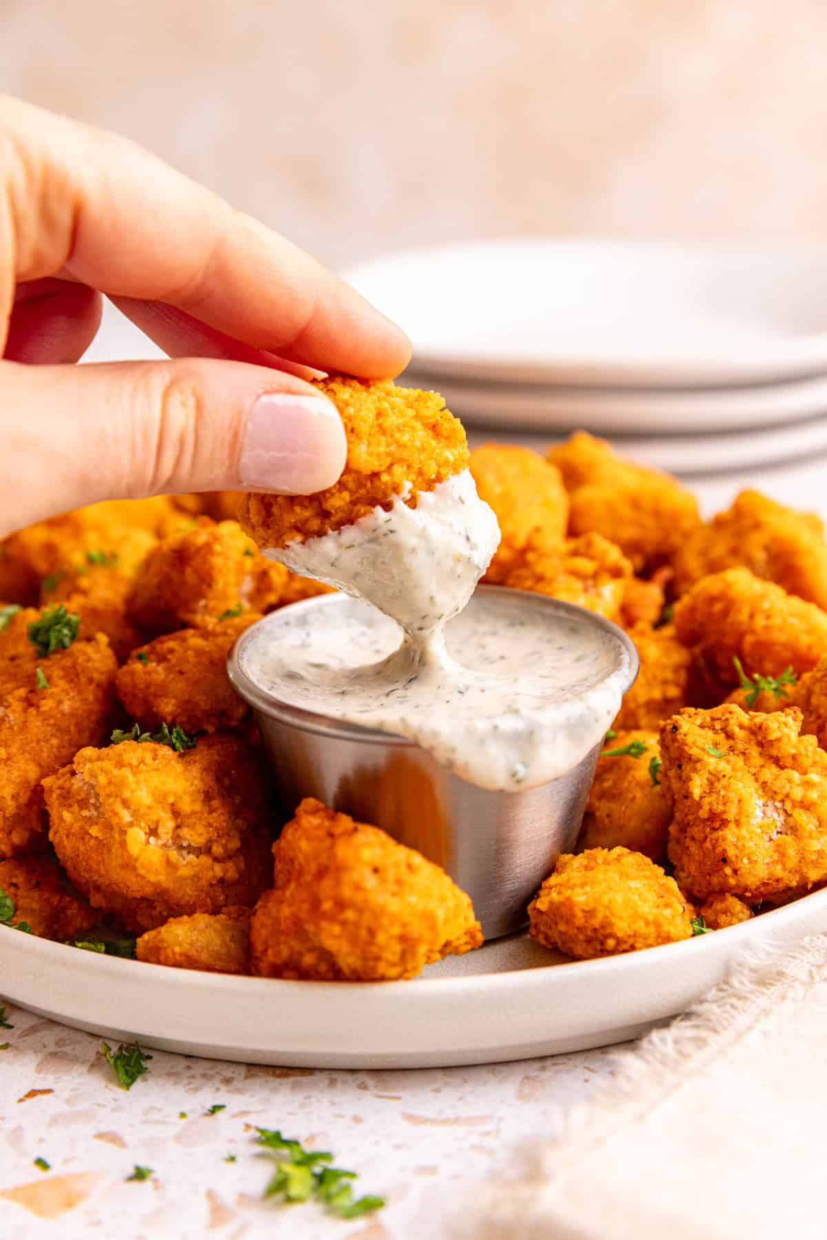 A hand dipping a popper into a dish of ranch.