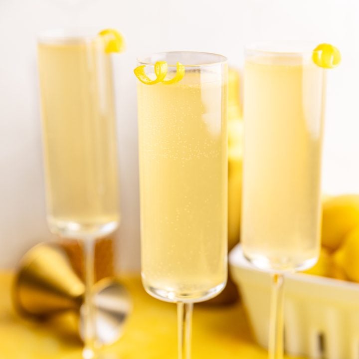 Three champagne glasses of french 75 mocktail, garnished with lemon twists.