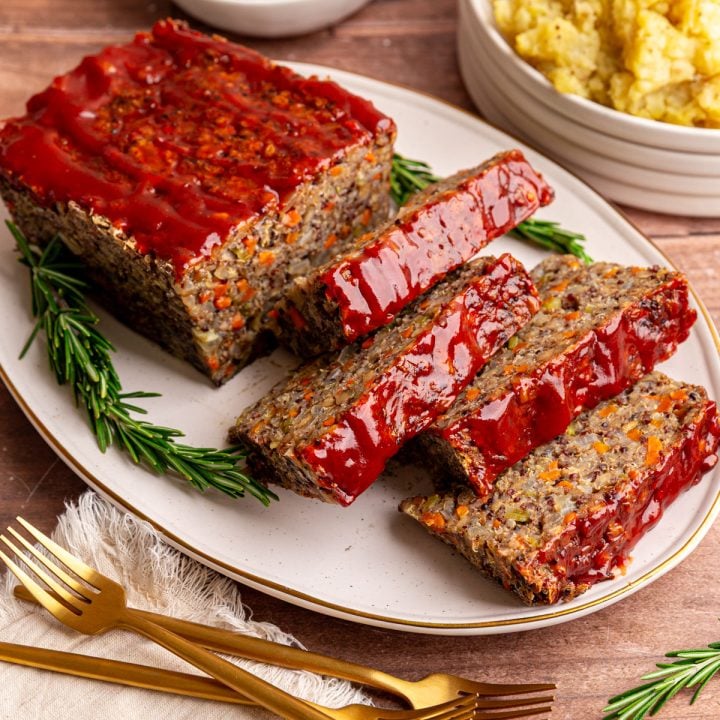 A sliced lentil quinoa loaf on a platter, with rosemary on the platter, and mashed potatoes in the background.