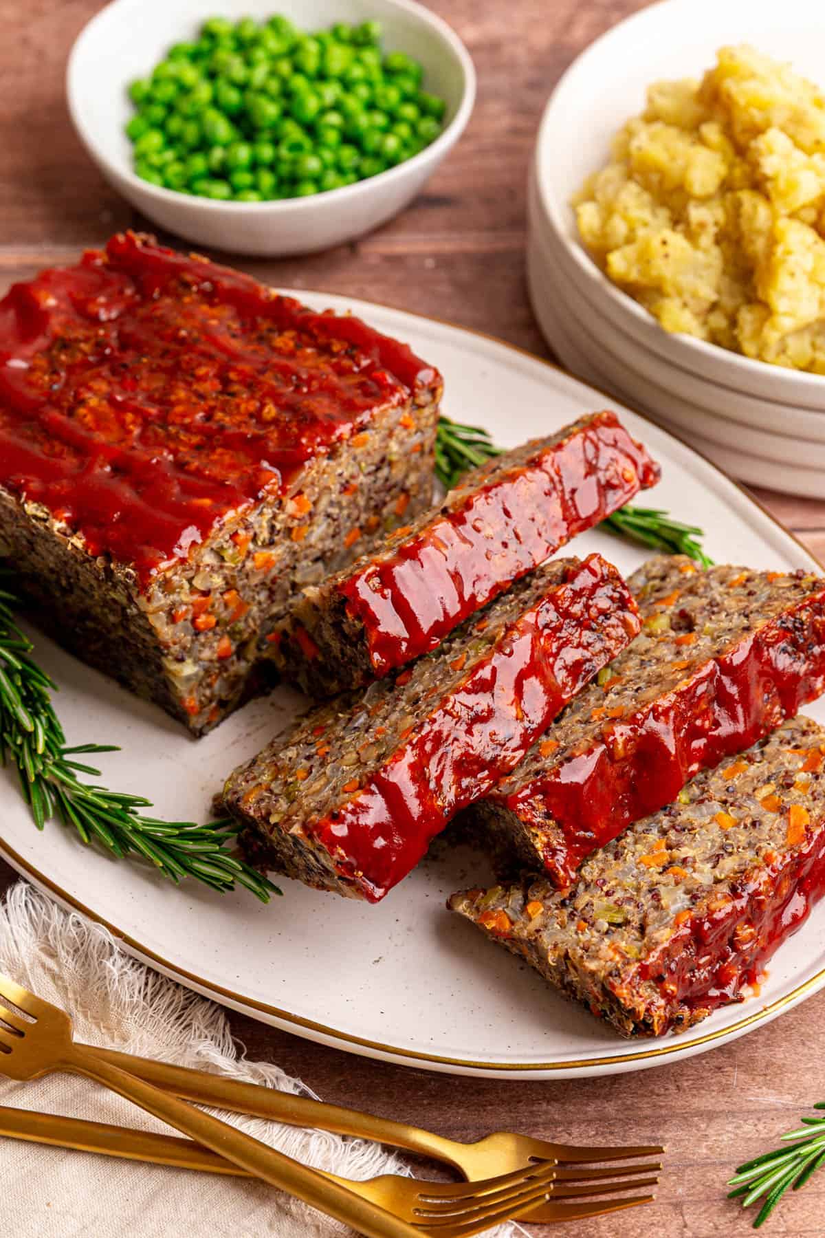 A sliced lentil quinoa loaf on a platter, with rosemary on the platter, and mashed potatoes in the background.