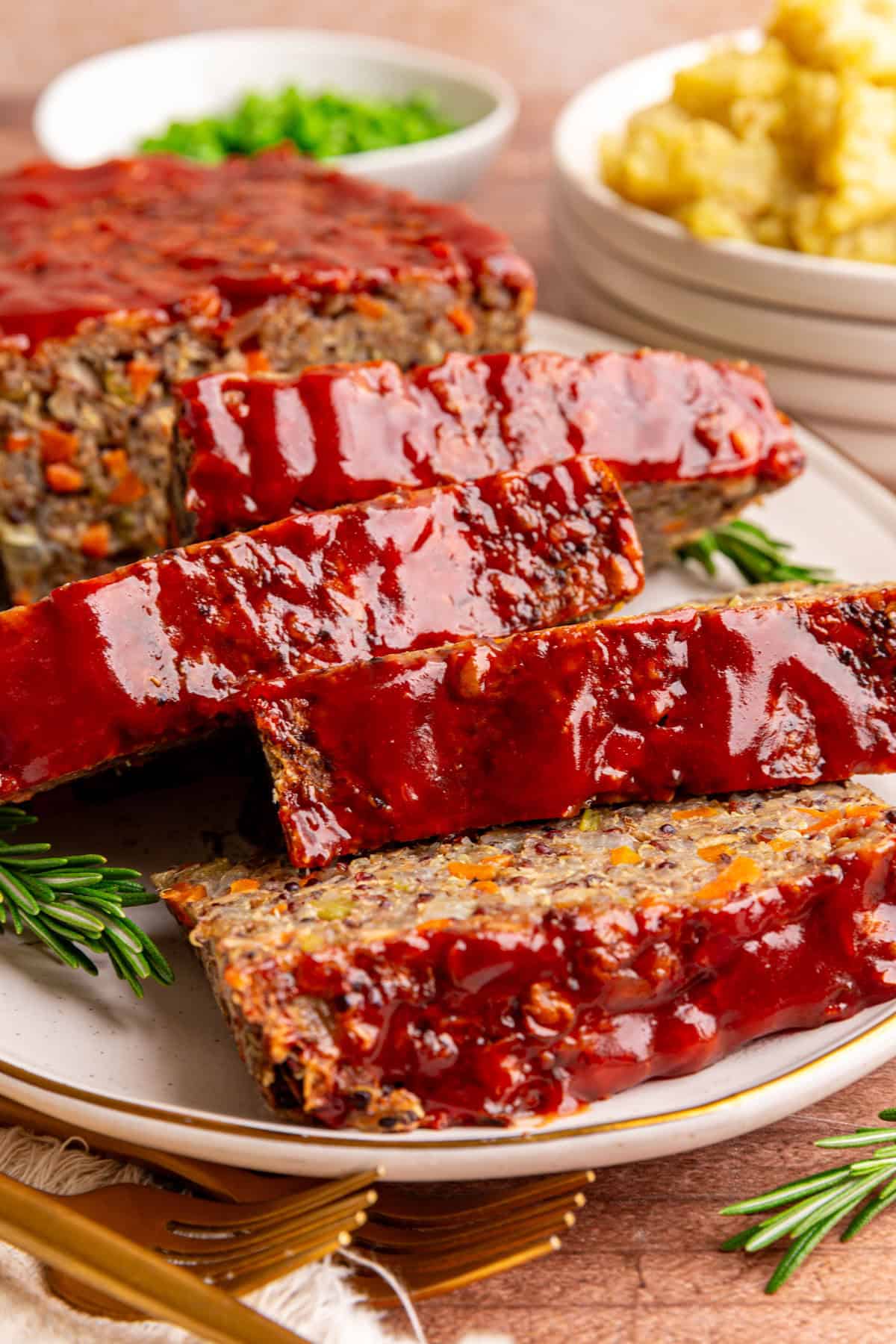 A sliced lentil quinoa loaf on a platter, with rosemary on the platter, and mashed potatoes in the background.