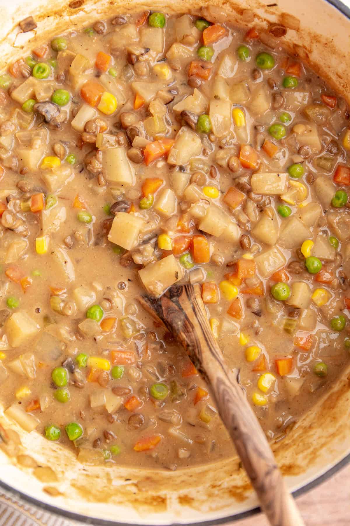 A pot of freshly cooked vegan shepherd's pie soup, with a wooden spoon.