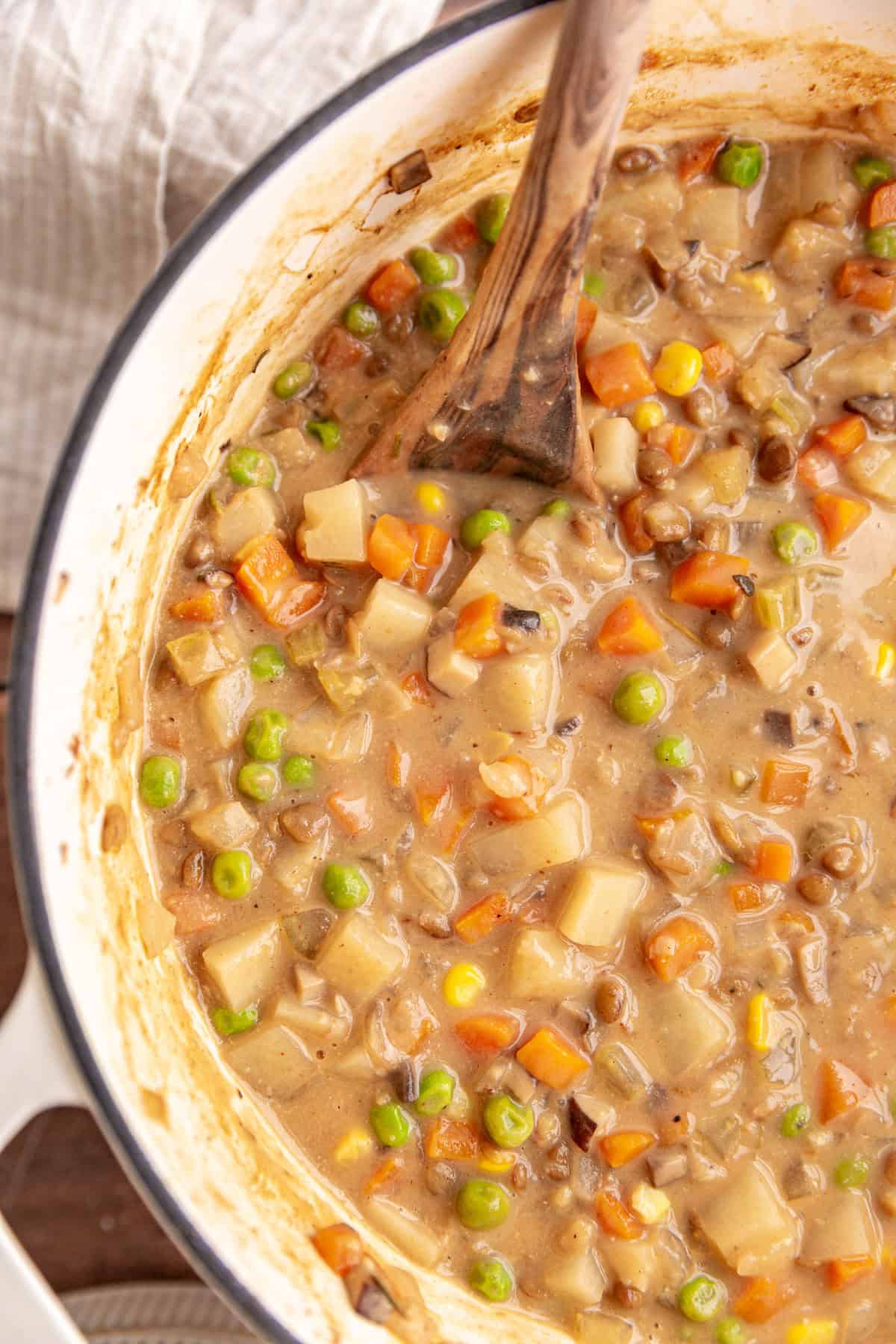 A pot of freshly cooked vegan shepherd's pie soup, with a wooden spoon.