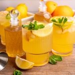 A few glasses of citrus mocktail on a table with jars of lemon ginger syrup.