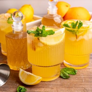 A few glasses of citrus mocktail on a table with jars of lemon ginger syrup.