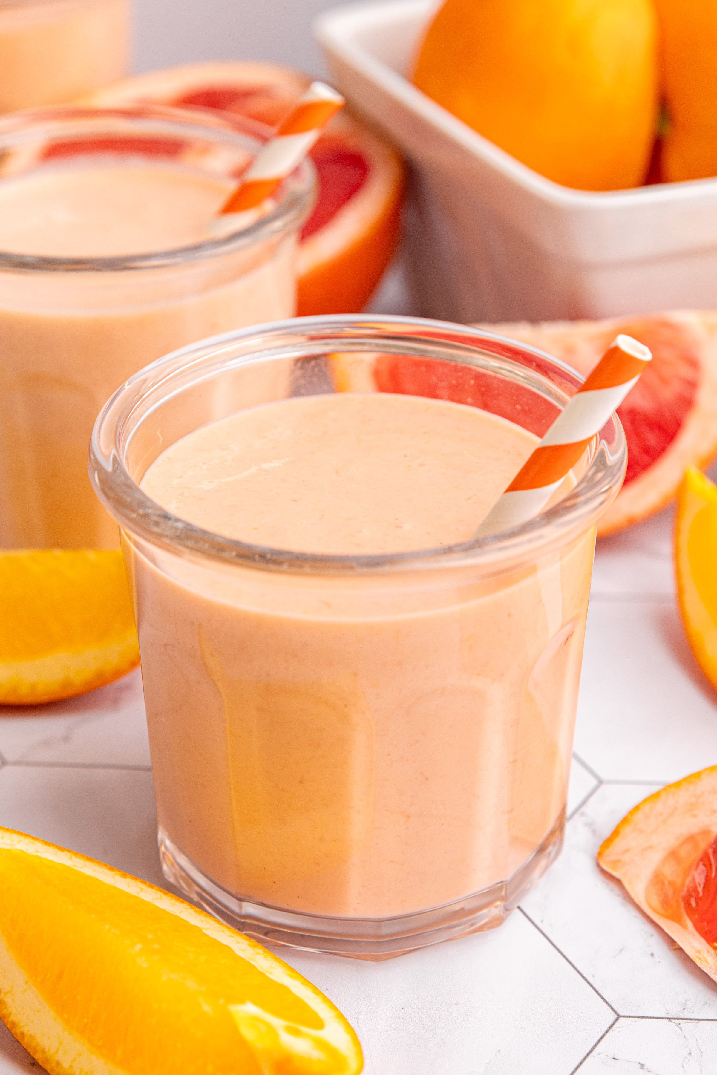 A glass of citrus smoothie with an orange and white striped straw.