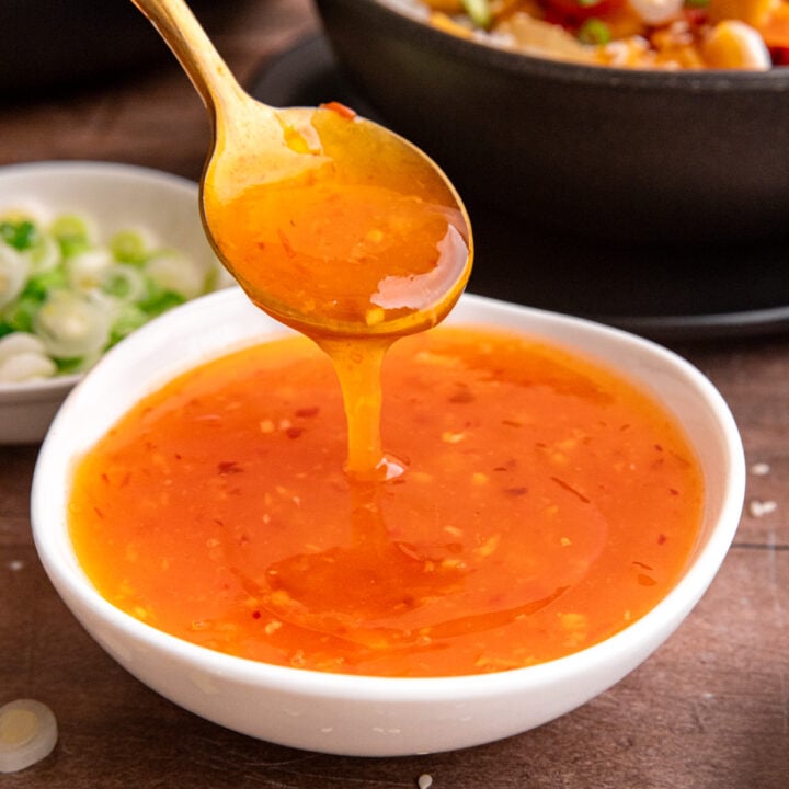 A spoon scooping a spoonful of sweet chili sauce.