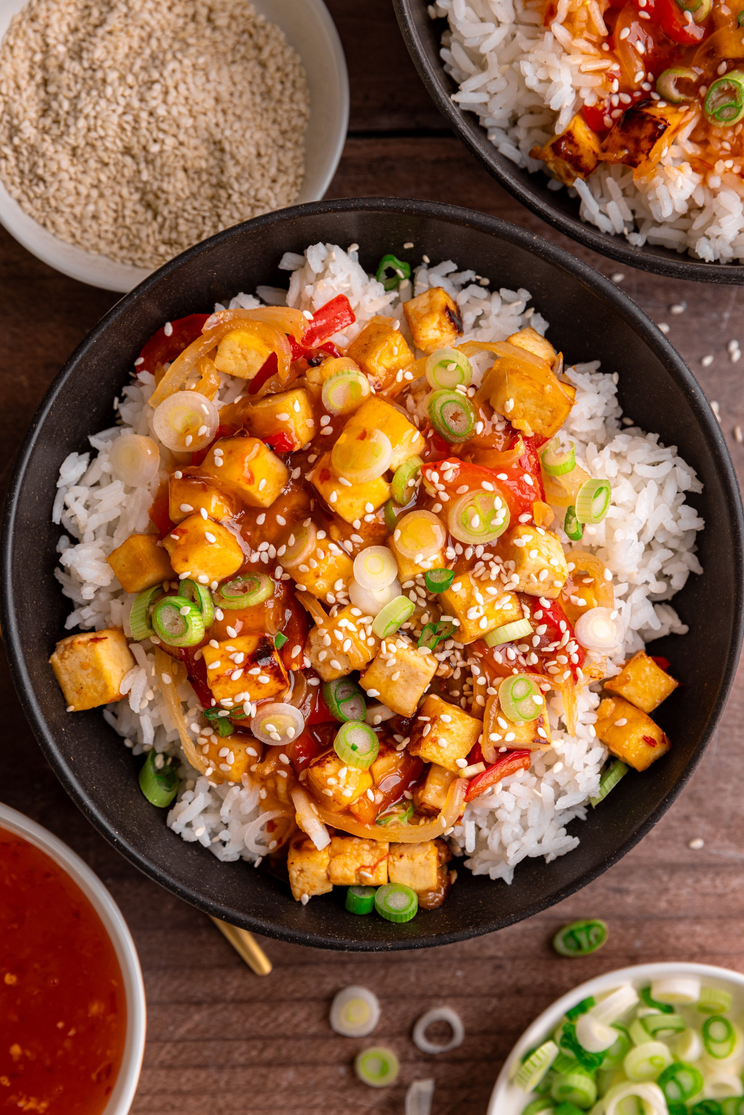A bowl of sweet chili tofu, over rice, topped with scallions and sesame seeds.