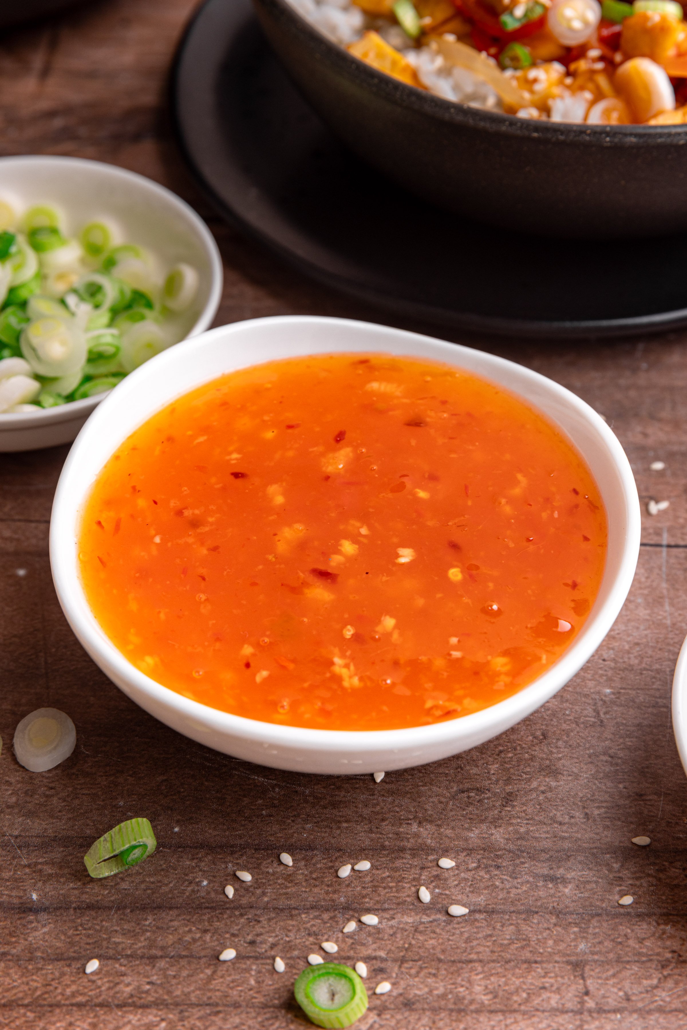 A bowl of sweet chili sauce, next to a bowl of sweet chili tofu.