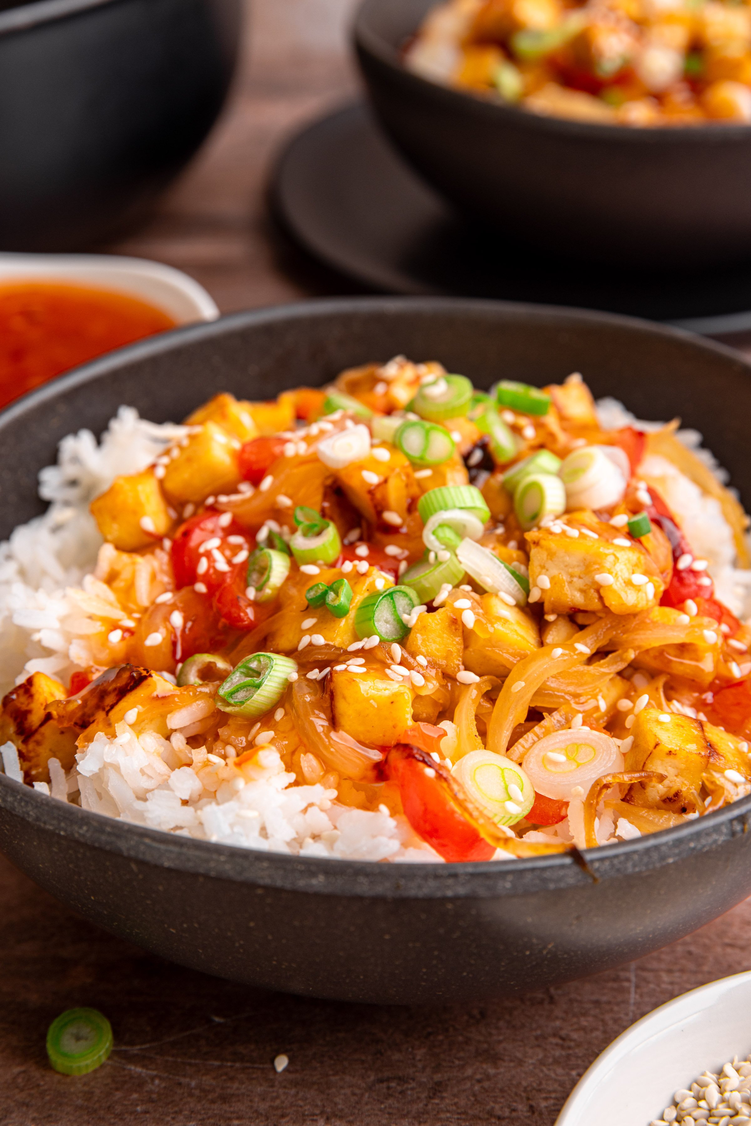 A bowl of sweet chili tofu, over rice, topped with scallions and sesame seeds.