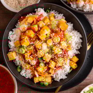 A bowl of sweet chili tofu, over rice, topped with scallions and sesame seeds.