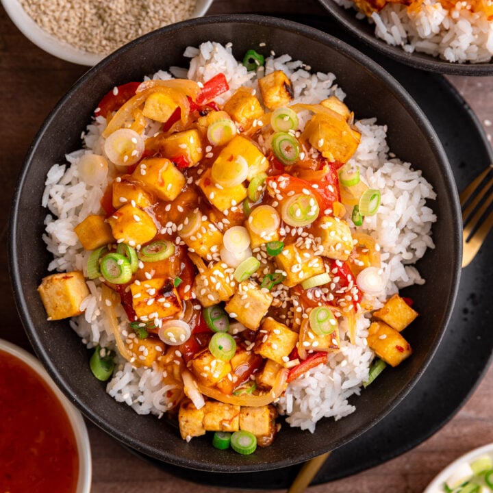 A bowl of sweet chili tofu, over rice, topped with scallions and sesame seeds.