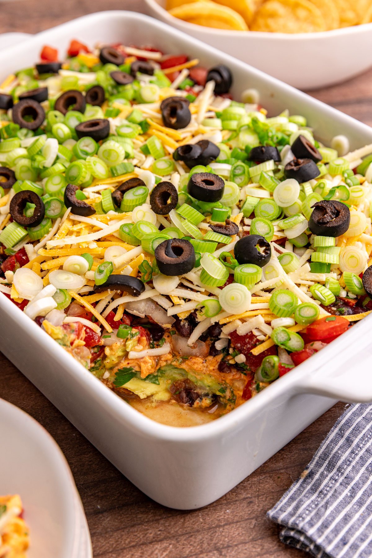 A dish of vegan 7 layer dip with a few bites scooped out to reveal all the layers.