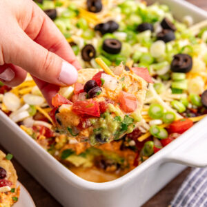 A hand scooping out a bite of vegan 7 layer dip with a tortilla chip.