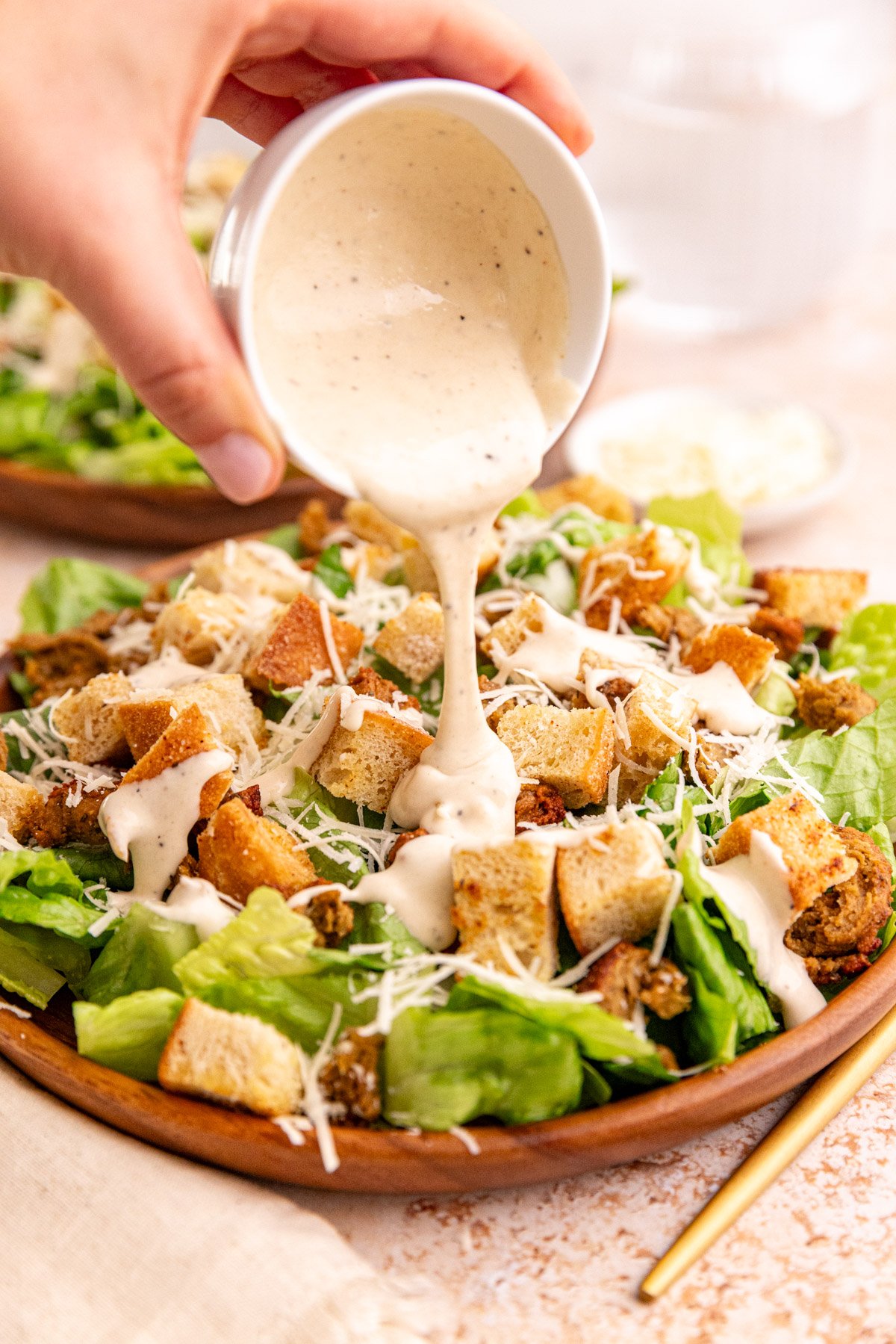 Dressing being poured onto a plate of vegan chicken caesar salad.