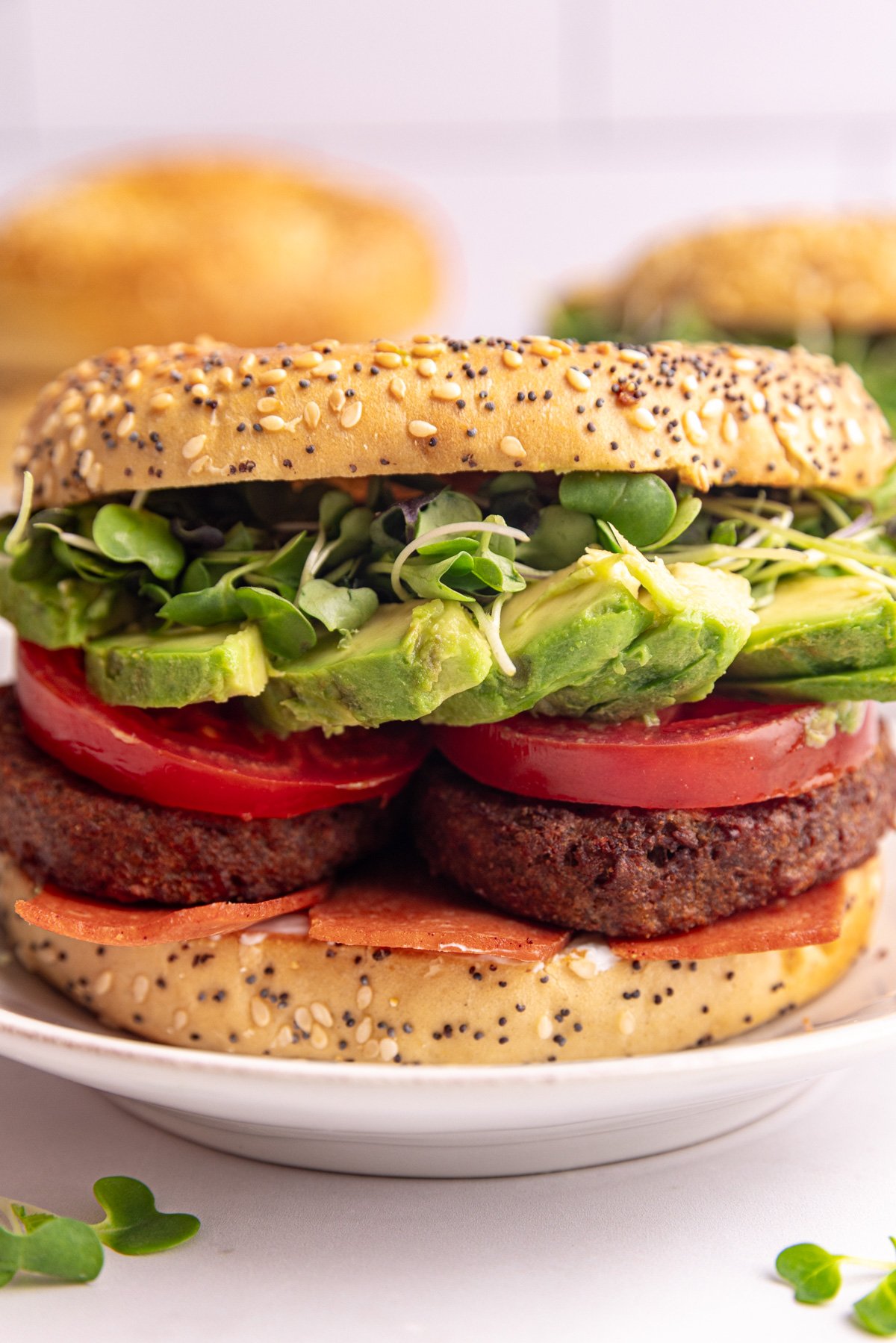 A vegan bagel breakfast sandwich, stuffed with vegan sausage, tomato, avocado, and microgreens.