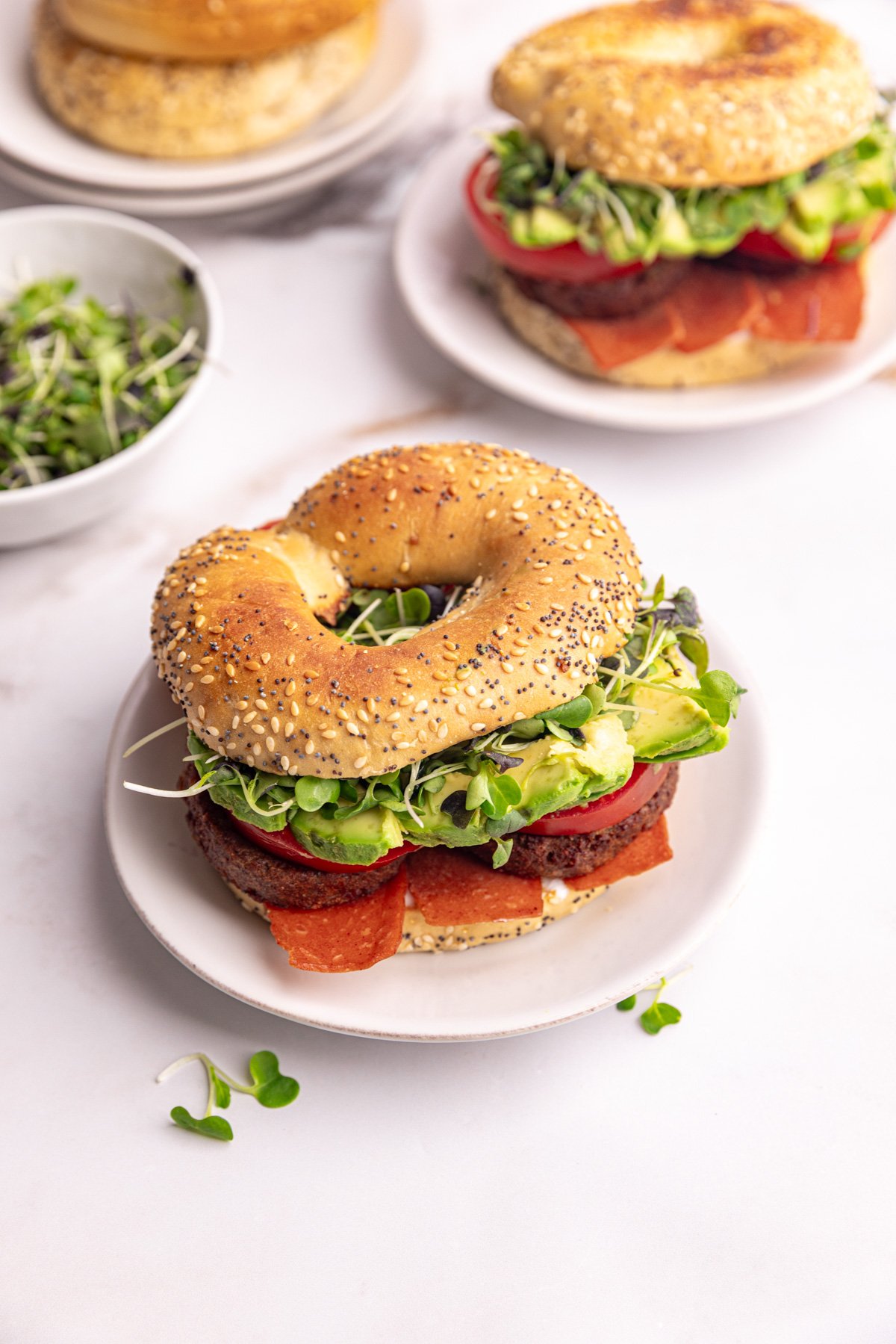 A vegan bagel breakfast sandwich, on a plate, ready to eat.