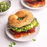 A vegan bagel breakfast sandwich, on a plate, ready to eat.