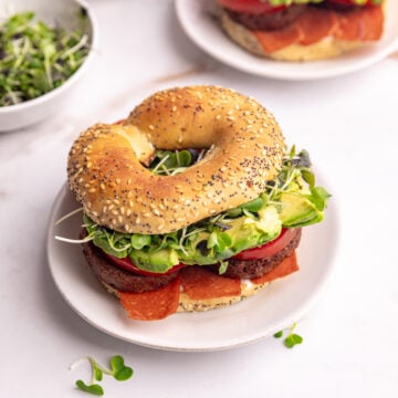 A vegan bagel breakfast sandwich, on a plate, ready to eat.