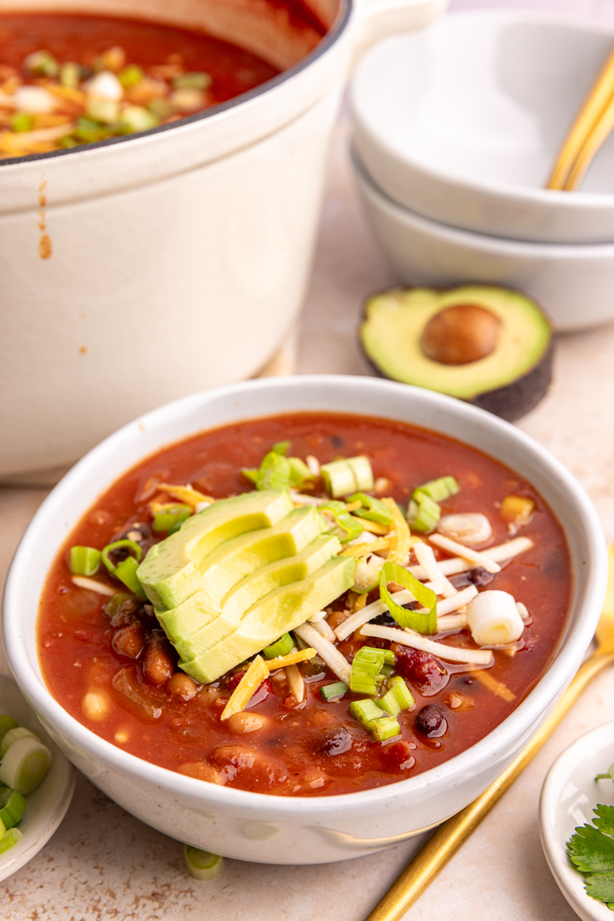 A bowl of vegan 5 bean chili garnished with avocado, vegan cheese, and scallions.