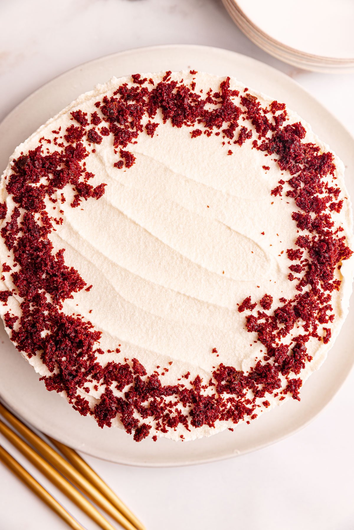 A whole vegan red velvet cake on a plate, decorated with cake crumbs.