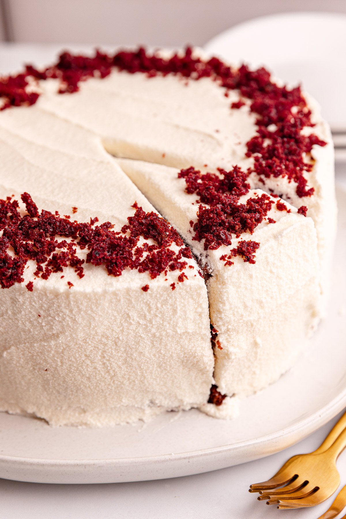 A whole vegan red velvet cake on a plate, with a slice cut, ready to serve.