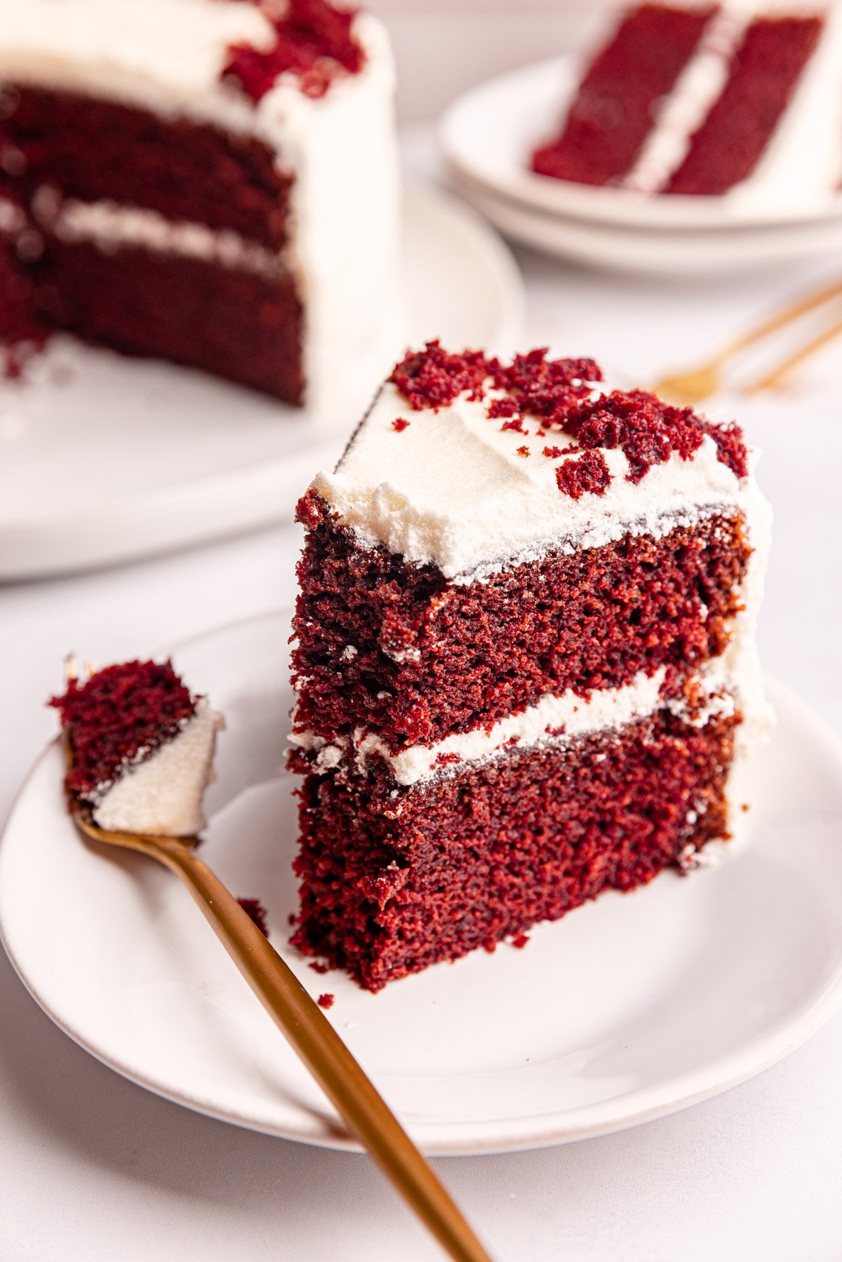 A slice of vegan red velvet cake standing on a plate with a bite removed.